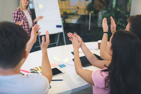 Cut view of people clapping in hands. They look at blonde woman standing near flipchart.の写真素材