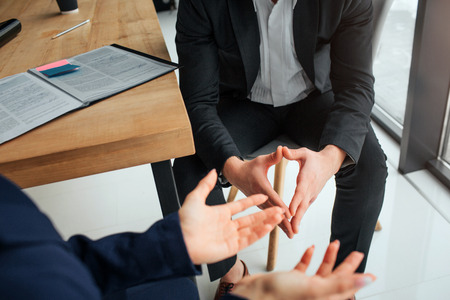 Cut view mans and womans hands. People sit in front of each other in meeeting room at table. They talk and have conversation.の写真素材