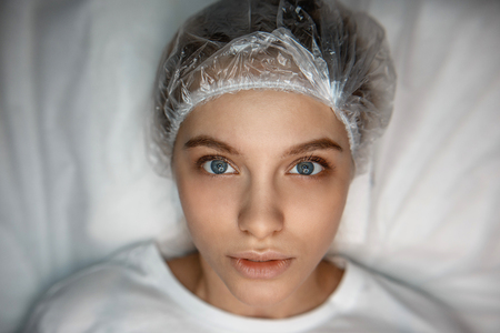 Young woman lying on couch and look on camera. She serious and concentrated. Lamp lightning her...