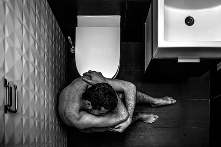 Painful picture of young man sitting on floor in rest room and suffer. He is naked and lonely. Guy has problems. He cry and feel exhaustion.の写真素材