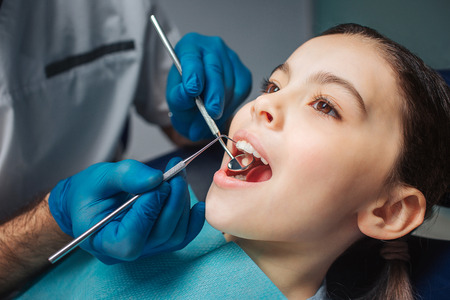 Calm peaceful girl sit in dental chair in room. She keep mouth opened. Dentist use tools for check up.の写真素材