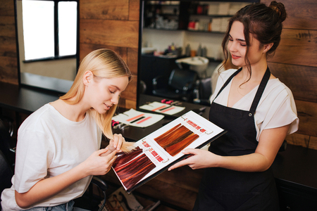 Young beautiful woman and hairdresser comparing her blonde hair with color hair from palette before correct coloring. Beauty, hair dyeing conceptの写真素材
