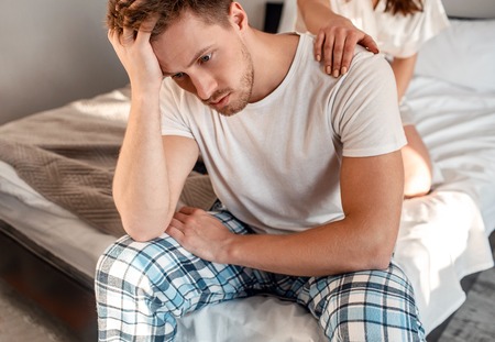 Young couple in the bed. Close-up of unhappy man is sitting on the edge of bed, problem in the bedroomの写真素材