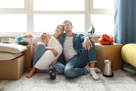 Young family couple bought or rented their first small apartment. Two people sit on floor and look...