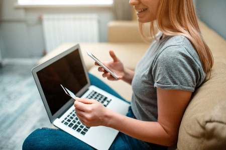 Online shopping at home. Young smiling shopper with a credit card, smartphone, laptop is ready for...