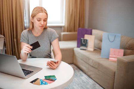 Online shopping at home. Young blonde shopper with laptop and credit card is paying in online shop while sitting at the tableの写真素材