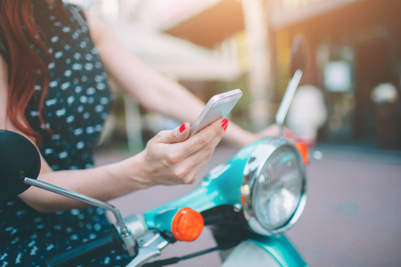 Beautiful young woman dressed casual sitting on scooter and talking on phone. Girl sitting on the bike and using Cellular smartphoneの写真素材