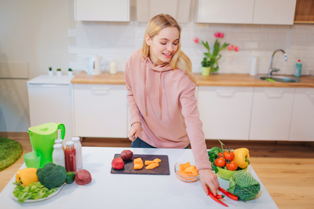 Vegan beautiful blonde woman cooking raw vegetables in the kitchen. Raw food diet. Vegetarian food. Healthy eatingの写真素材