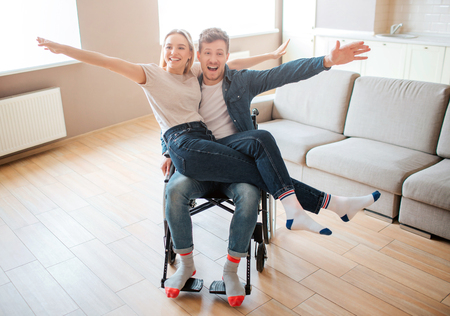 Young man with disability and inclusiveness holding girlfirend on knees. They smile and pose on camera. Cheerful happy couple.の写真素材