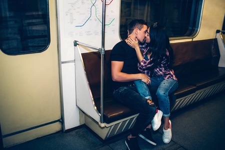 Young man and woman use underground. Couple in subway. Kissing scene on bench in metro carriage. Embrace and cheerful hug. Love at first sight.の写真素材