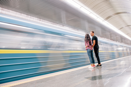 Young man and woman use underground. Couple in subway. Stand at edge of platform. Hand in hand. Love in air. Together in metropolitan.の写真素材