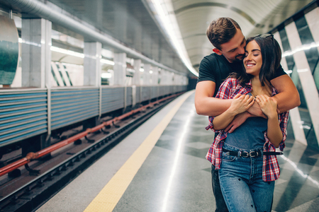Young man and woman use underground. Couple in subway. He stand behind her and embrace. Kissing scene. Cheerful young woman smile. Love story.の写真素材