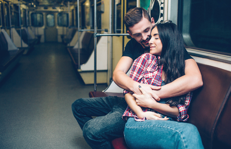 Young man and woman use underground. Couple in subway. Sitting on bench and embrace each other. Happiness and love.の写真素材