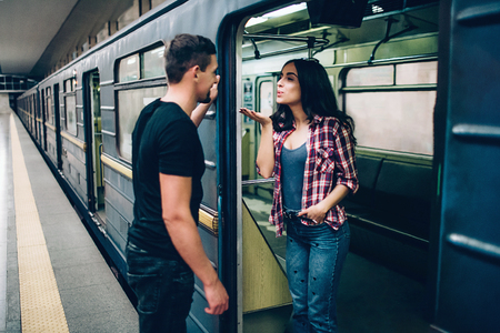 Young man and woman use underground. Couple in subway. Lovely young woman send kisses to man. Guy look at her and smile. Together alone on platform and underground carriage.の写真素材