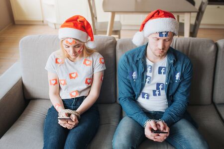 KYIV, UKRAINE - APRIL 26, 2019: Facebook logo.  illustration. Facebook icon. Young man and woman have social media addiction. Christmas holiday concept. Hostages of social media.のeditorial素材