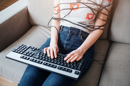Young woman have social media addiction. Cut view. Typing on keyboard. Body wrapped with cord. Addictiveness from laptop or smartphone.の写真素材