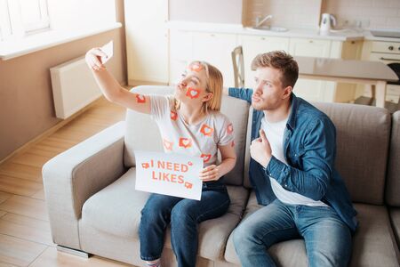 KYIV, UKRAINE - APRIL 25, 2019: Facebook logo.  illustration. Facebook icon. Young man and woman have social media addiction. Taking selfie using phone. Posingo n camera together in room on sofa.のeditorial素材