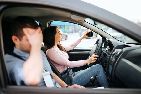 Male auto instructor takes exam in young woman. Shamed guy cover face with hand. Female student...