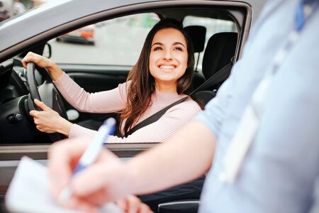 Male auto instructor takes exam in young woman. Cheerful attractive model look at guy and smile....