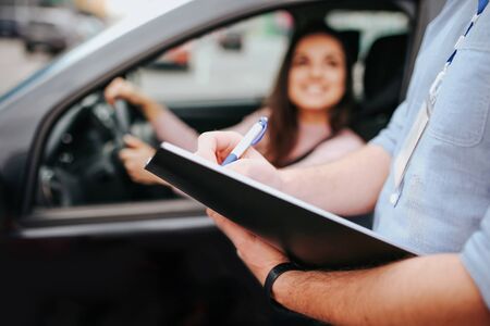 Male auto instructor takes exam in young woman. Blurred background of model sitting in car and...