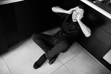 Black and white picture of young man in black clothes sitting separated alone in kitchen and scream....