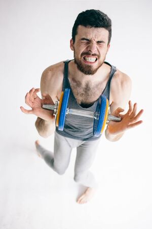 Skinny man training his bicep muscle. Guy lifting one dumbbell. young student training to become strongerの写真素材