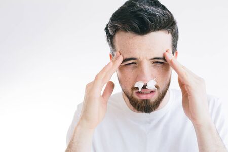 Portrait of young sick man with headache holding forehead in pain. Nose sneezing. Coronavirus. Brunette bearded man isolated over background.の写真素材