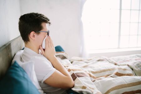 young man with handkerchief. Sick guy on the bed has runny nose. man makes a cure for the common...