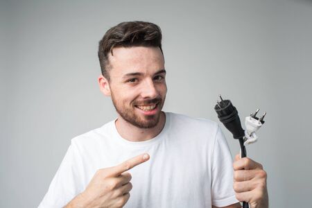Young man isolated over background. Guy repair master hold cord with socket in hand and point on it....