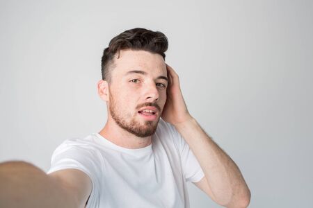 Young man isolated over background. Guy hold camera and take selfie. Posing alone with pleasure. Hold one hand on ear. Mysterious and emotional.の写真素材