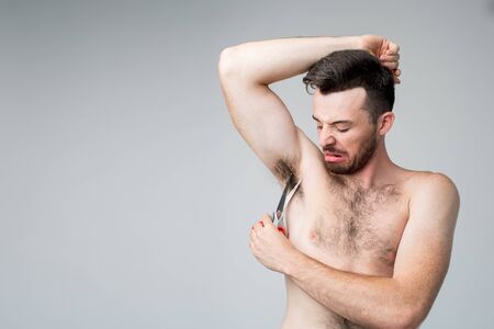 Young man isolated over background. Close up of guy trying to cut hair under his armpit. Advertising concept. Try to do it best and alone.の写真素材