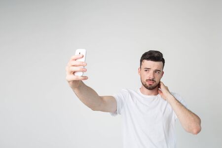 Young man isolated over background. Take selfie using smartphone in his hand. Stand alone and pose....