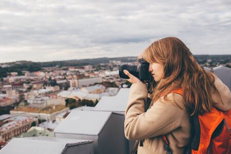 Beautiful female photographer taking pictures of old town. Tourist or female traveller have professional camera. Alone on top of tower. Urban view.の写真素材