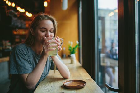 Young blonde in a cafe. She holds a cup in her hands and drinks aromatic teaの写真素材