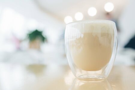Cappuccino latte or coffee with milk in modern glass with double bottom. Close-up view. Reflection...
