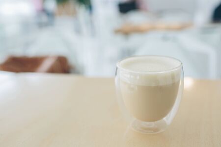 Cappuccino latte or coffee with milk in modern glass with double bottom. It on table. Close-up view. Blurred cafe on background. There is place for text.の写真素材