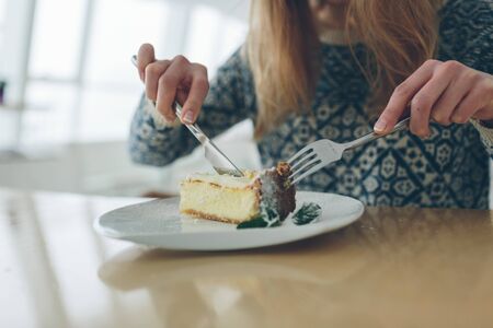 Closeup of cheesecake and leaf of mint sprinkled powder sugar on white plate. Cut view of blonde...