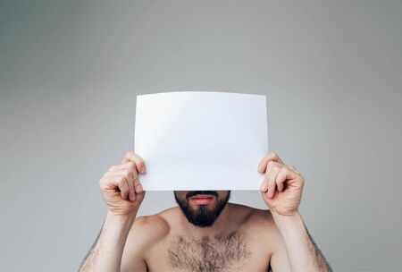 Young man isolated over background. Portrait of male person or model cover face with white blank page. Low part of face is not hidden. Brunette pose on camera.の写真素材