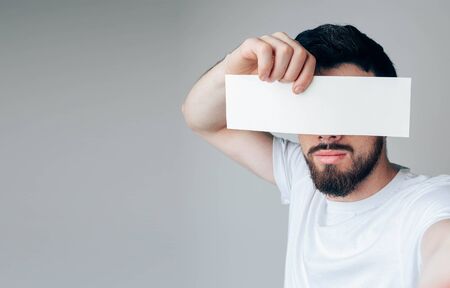 Young man isolated over background. Side view and selfie of bearded guy hide eyes from camera. Hold...
