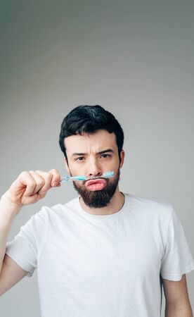 Young man isolated over background. Vertical picture of serious funny peaceful guy playing with toothbrush. Hold it between mouth and nose. Healthcare concept.の写真素材
