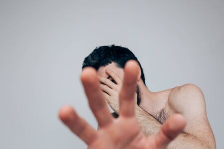 Young man isolated over background. Picture of guy cover face with hand and show another close to camera. Hide from sickness and mental emotional disorder. Confusion and concerning.の写真素材