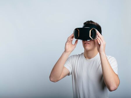 Joyful young man using VR headset for experiencing virtual reality. Stand alone in room and isolated...