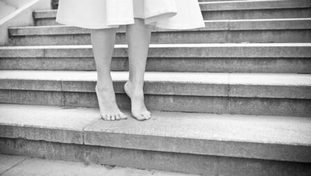 Balck and white picture of young woman walking barefoot outdoors. Close up low angle side view of female model in dress make step forward.の写真素材
