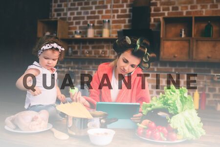 Mum at home. Young mother with little child in the home kitchen. Woman doing many tasks while looks after her baby. Use a tablet PC. Technology and Maternity.の写真素材