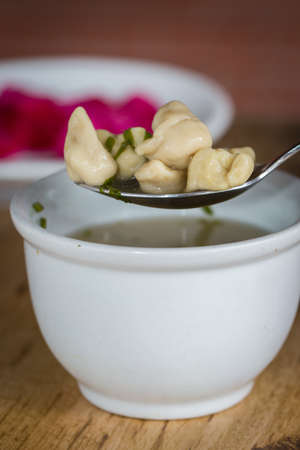 spoon with capeletti broth served in bowl, on wooden background.の写真素材