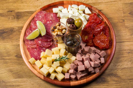 round board with various antipasti appetizers. Cheese, salami, olives, nut mix and sun-dried tomatoes. top view.の写真素材