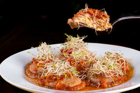 fork picking up vegetarian ravioli with tomato sauce and sprouts of white dishes. black background.の写真素材