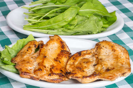 grilled chicken breast with arugula salad on top of checkered tablecloth.の写真素材