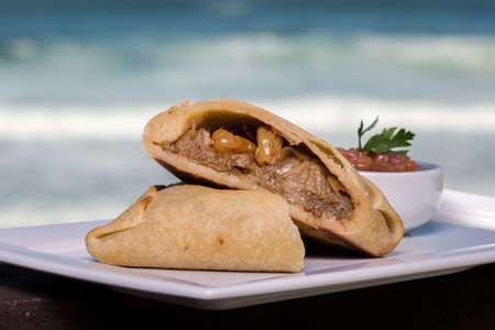 Traditional baked Argentinian empanadas with meat filling on white plate on wooden counter top with sea background.の写真素材