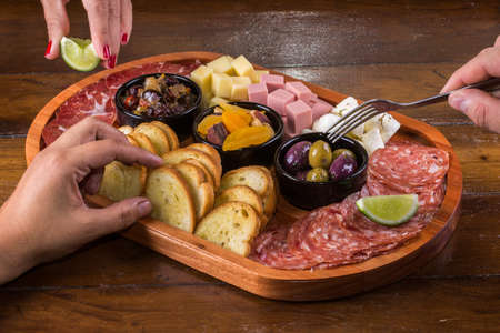 People eating wooden cutting board with cheese, cold cuts and jams.の写真素材